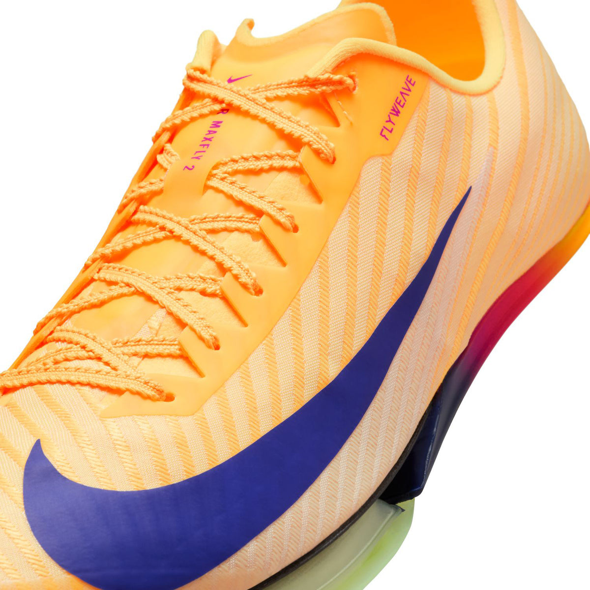 Close-up of an orange Nike athletic shoe with purple swoosh, gradient sole, and visible text FLYWEAVE near the laces. The shoe features striped detailing and colorful lace eyelets.