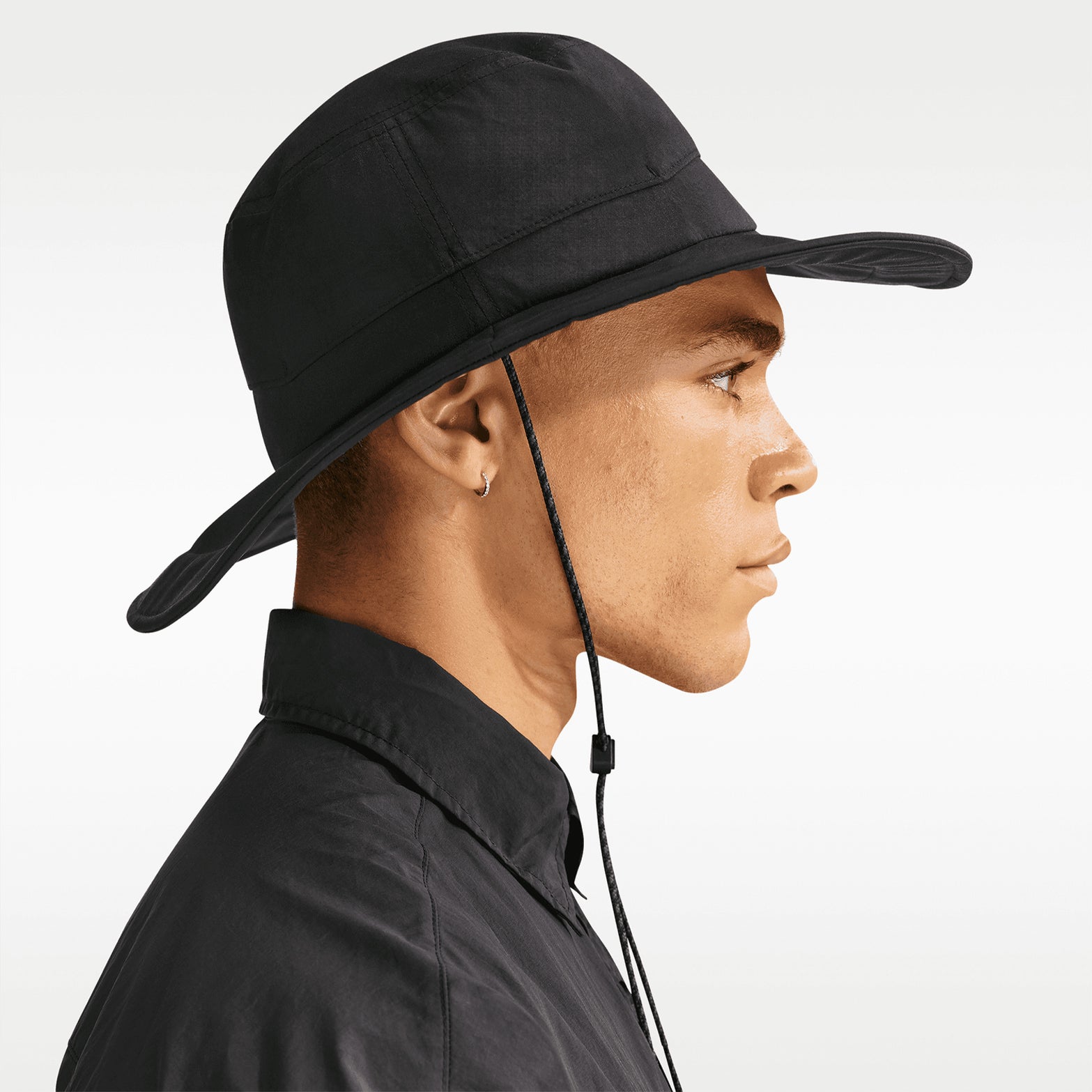 Nike ACG Apex bucket hat in Black — side view worn on male model showing black water-repellent taffeta fabric, extended wraparound brim and structured hat design