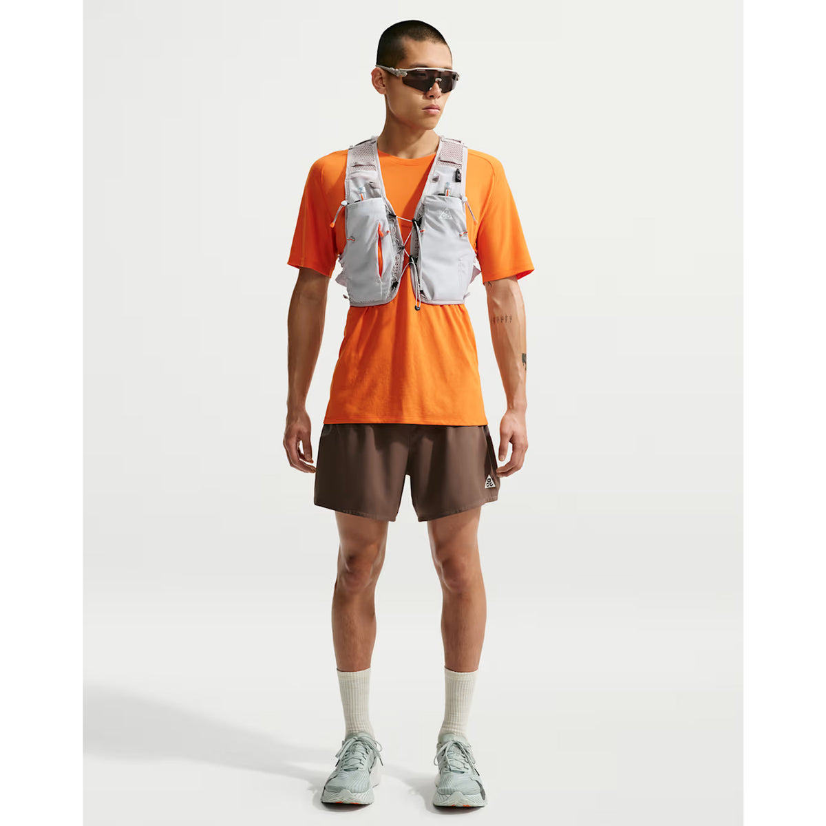 Nike ACG Goat Pack 5L Vest in Grey Fog / Safety Orange / Summit White — full body view worn on model showing complete 5L capacity, grey fog DyneemaⓇ mesh base with safety orange and summit white detailing in motion