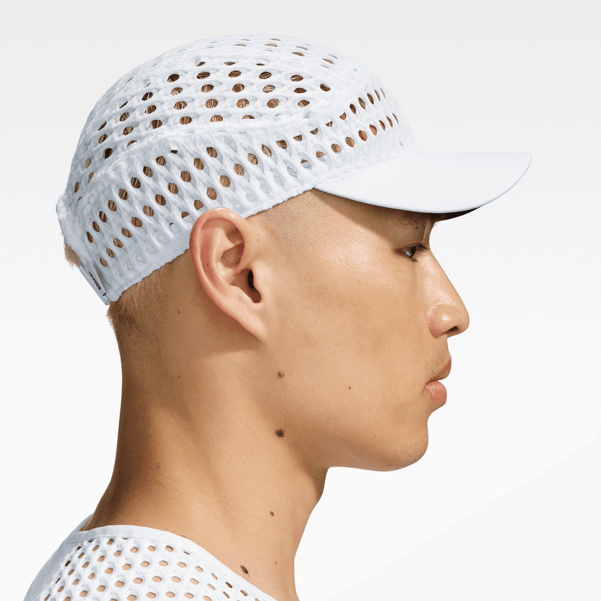 A person wearing a white Nike ACG Radical AirFlow Fly Cap made of perforated, mesh-like material.