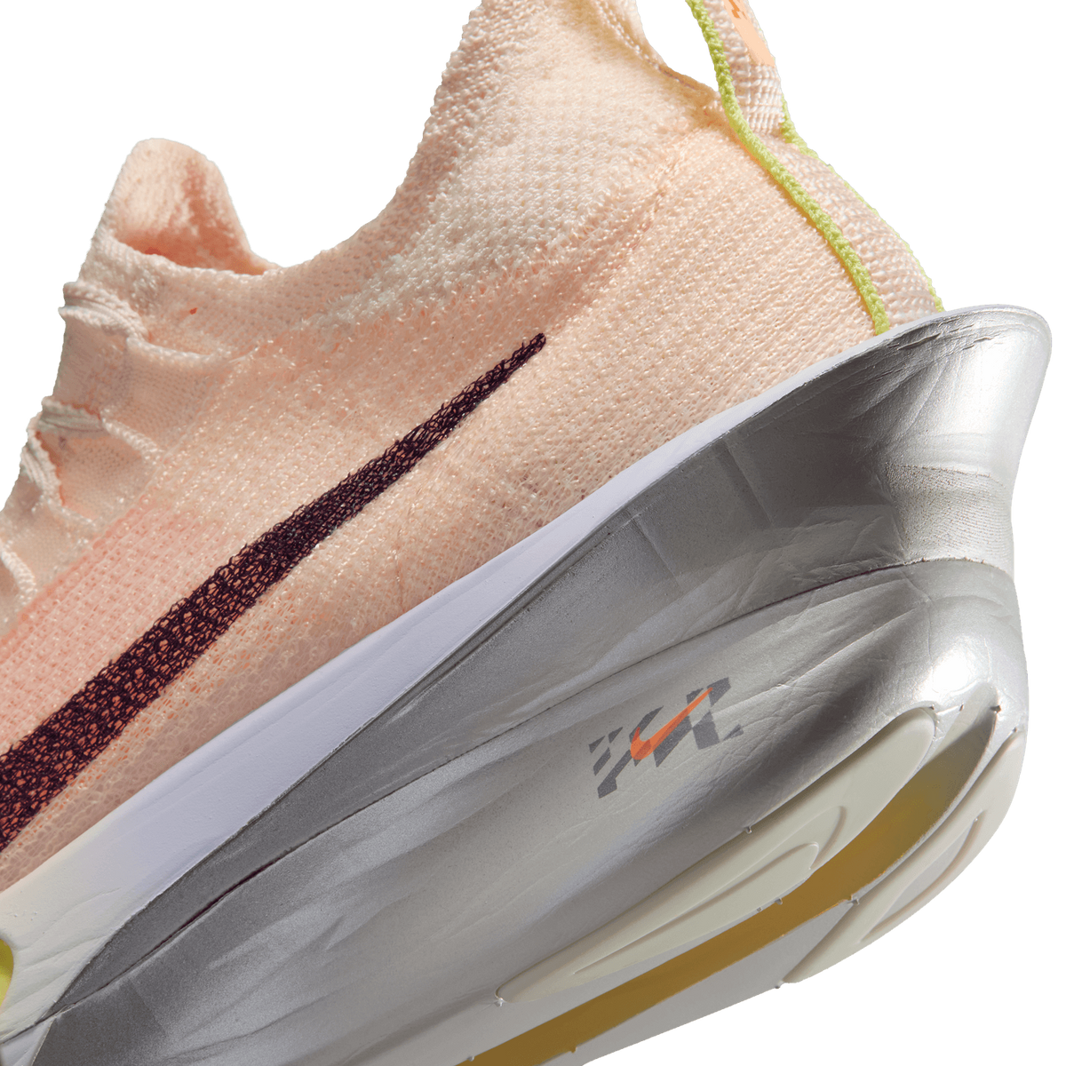 Close-up of a peach-colored athletic shoe with a maroon Nike swoosh, thick white and silver sole, yellow accents, and visible stitching detail on a plain background.
