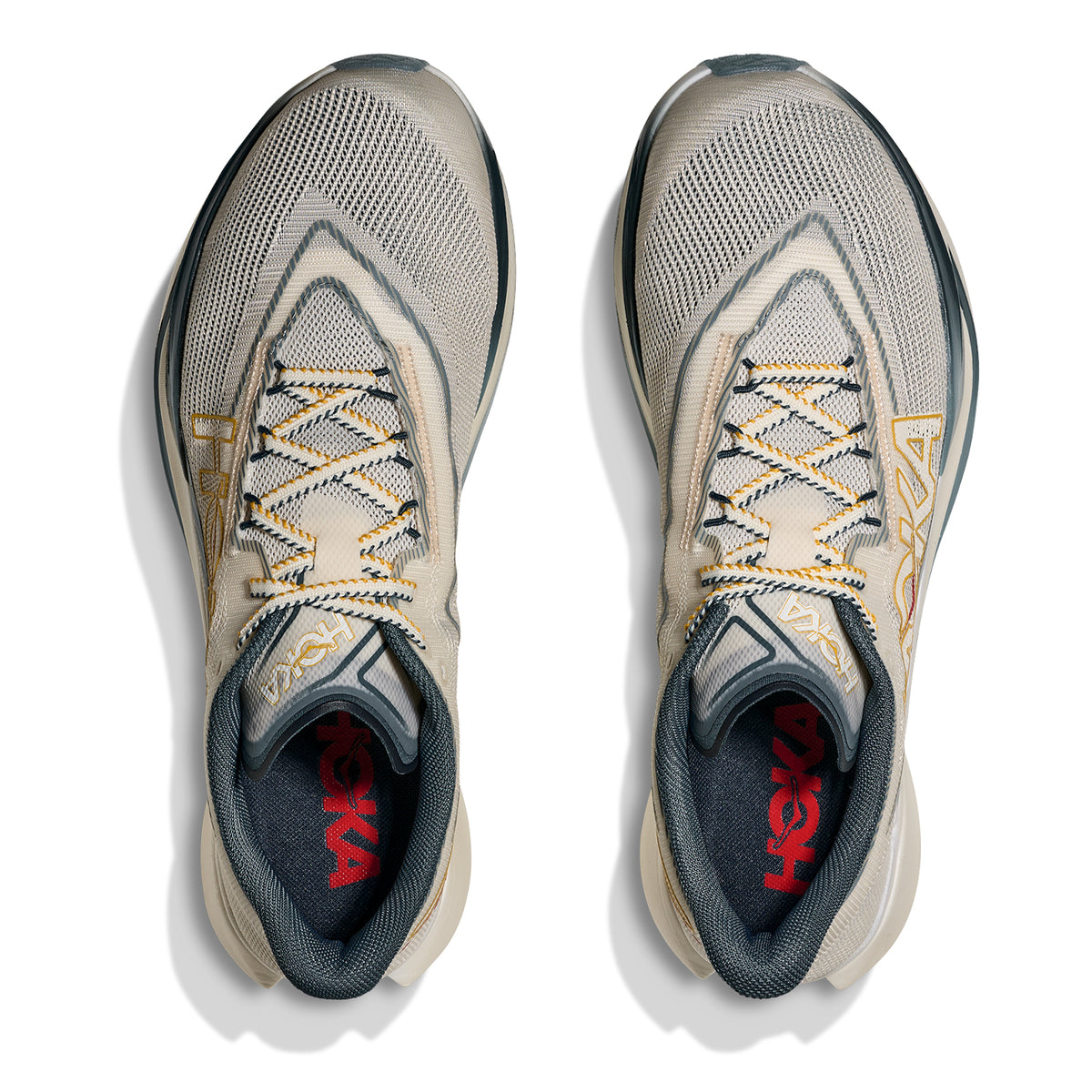 Top view of a pair of Hoka Cielo X1 3.0 Running Shoes in Alabaster / Yellow Gold, featuring black soles, yellow and black laces, breathable mesh uppers, and red Hoka branding on the insoles. Equipped with an advanced PEBA midsole for enhanced responsiveness, the shoes are neatly aligned side by side.