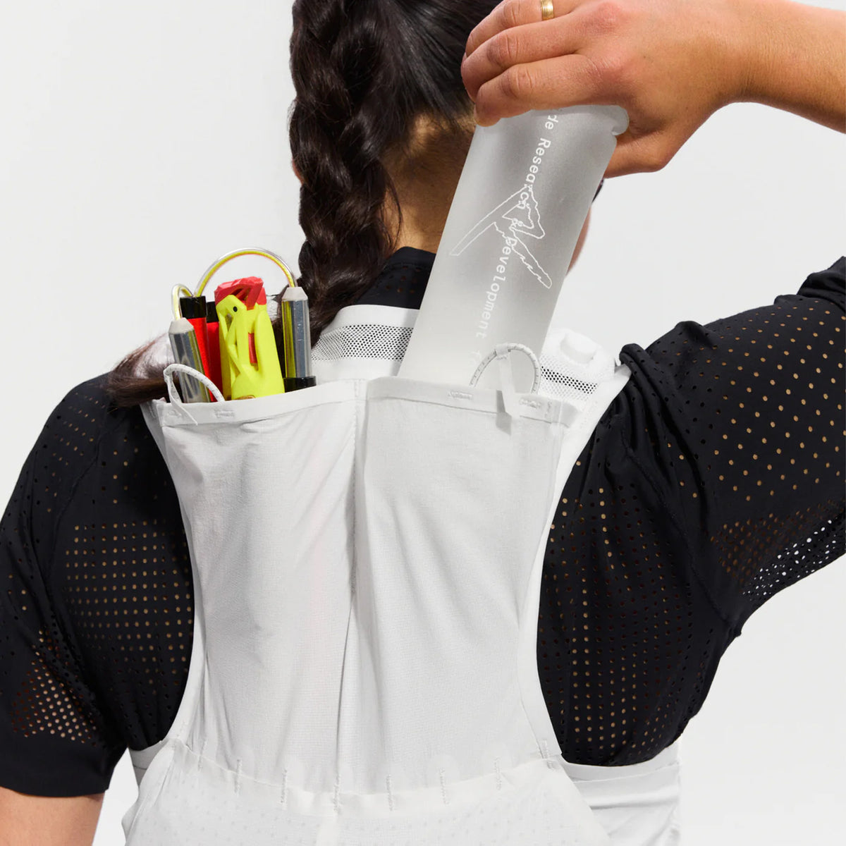 Raide LF 5L Running Vest in White — closeup showing 600ml Hydrapak locking flask being removed from rear hydration carry pocket with secure locking mechanism detail on white DyneemaⓇ mesh construction