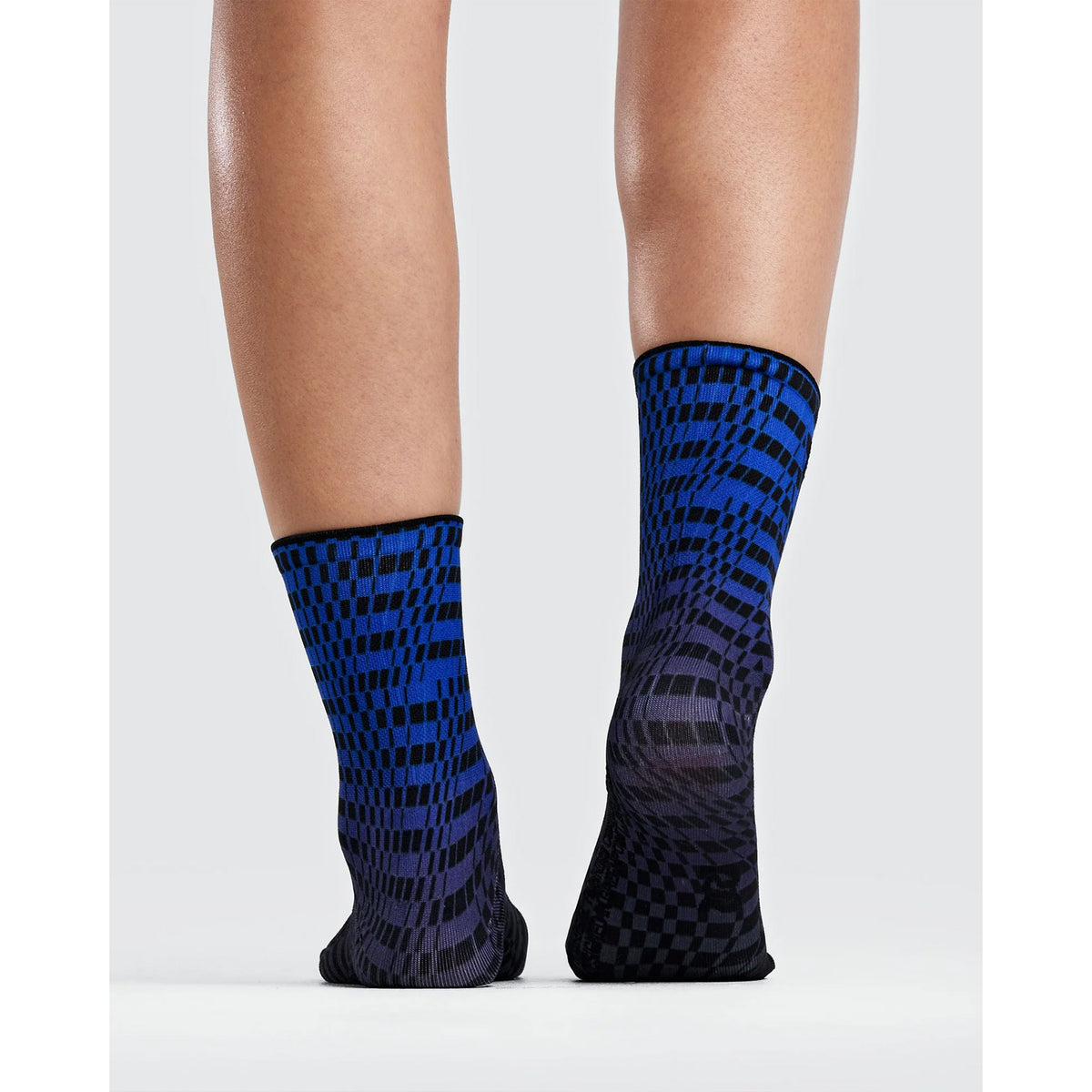 A pair of Bandit Lite Run 2 Pack Quarter Socks Bauhaus Blue featuring a blue and black checkerboard gradient pattern, worn on a person’s feet.