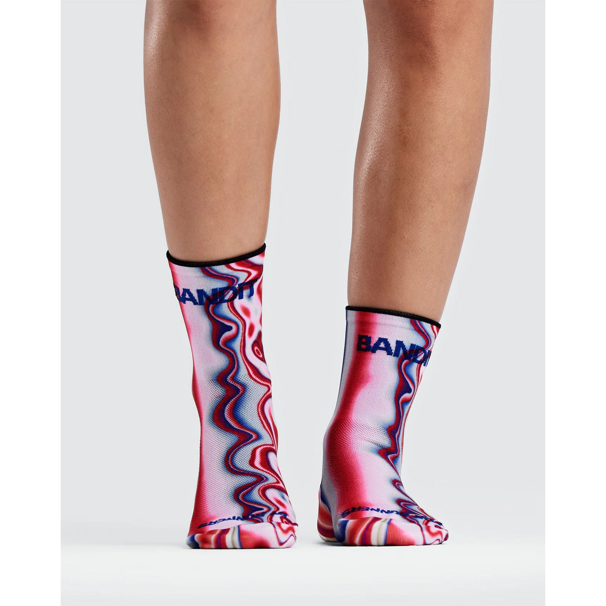 A person wears two Bandit Lite Run 2 Pack Quarter Socks Melted Stripe Gradient featuring a red, white, and blue melted stripe gradient pattern with a blue logo near the cuff.