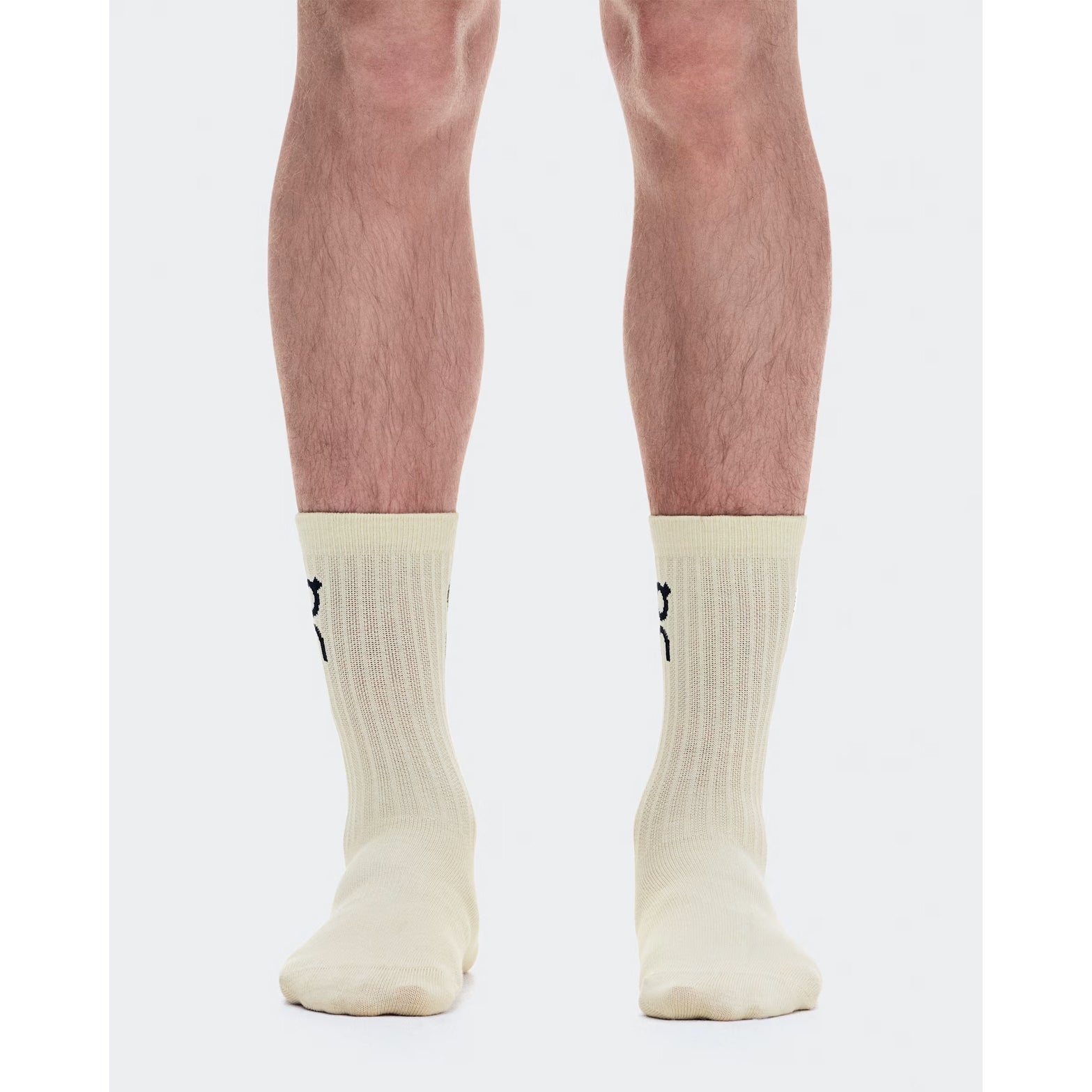 A person stands with feet together, wearing On’s Logo Socks High in the Hare / Brume colorway—off-white ribbed all-day comfort socks featuring a small black logo on the back—against a white background.