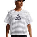 A person in the Nike Men’s ACG Radical AirFlow Tee White / Anthracite and a white cap looks to the side, showing tattoos on both forearms. The shirt features an ultra-breathable open-hole knit and black chest logo.