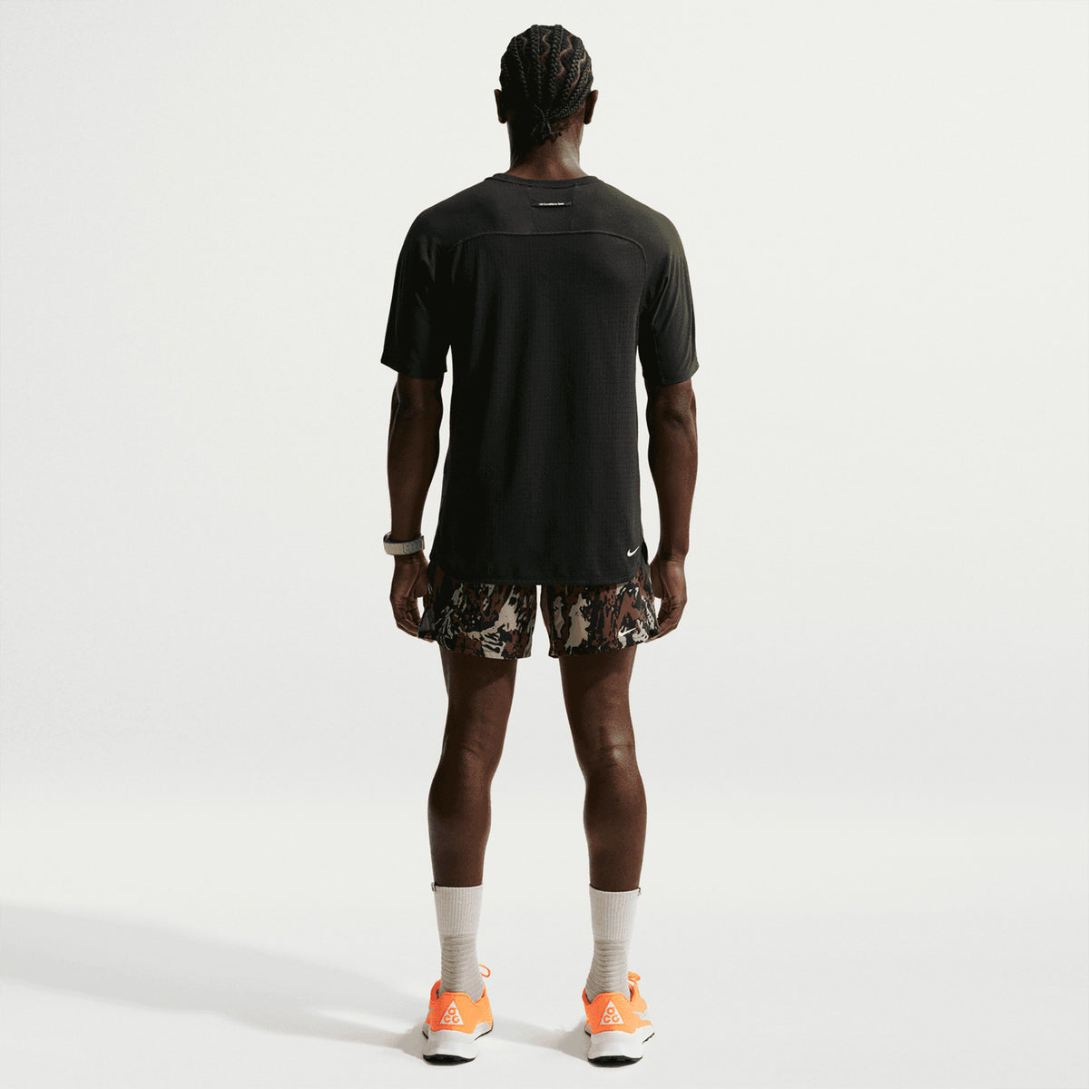 Men's Nike ACG Solar Chase Dri-FIT ADV Trail Running Tee Black Summit White full body back view on male trail runner showing strategic back mesh panels with Dri-FIT ADV moisture-wicking and reflective ACG branding for low-light visibility
