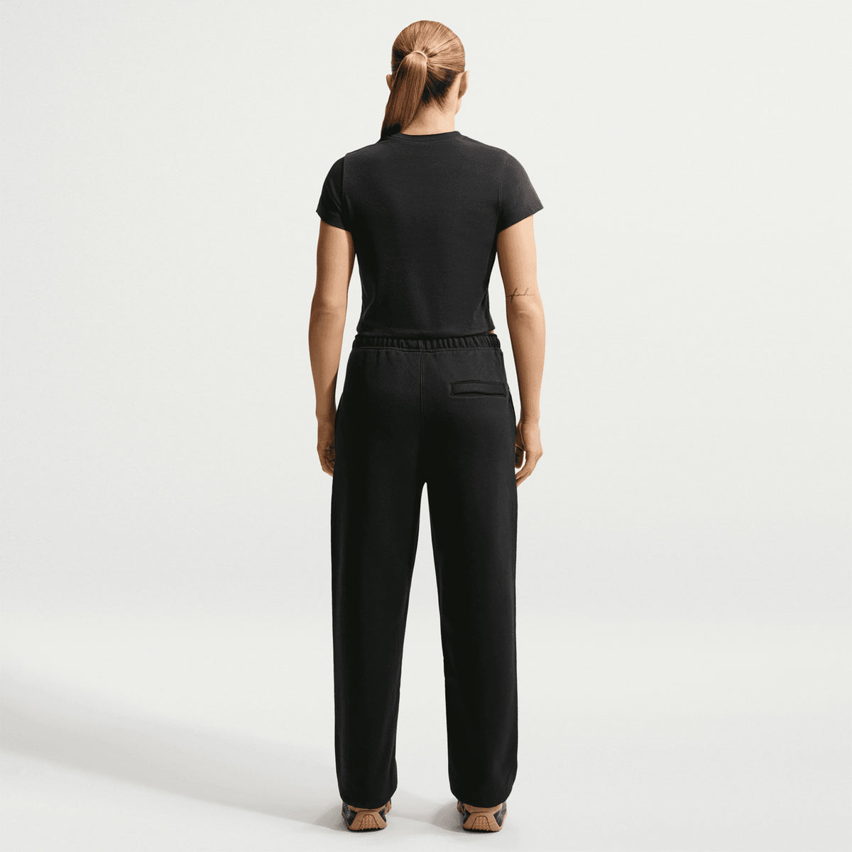 Nike ACG Tuff Fleece trousers in Black / Summit White — back view worn on female model showing black heavyweight fleece, elastic cuff detail and snap secure back pocket storage