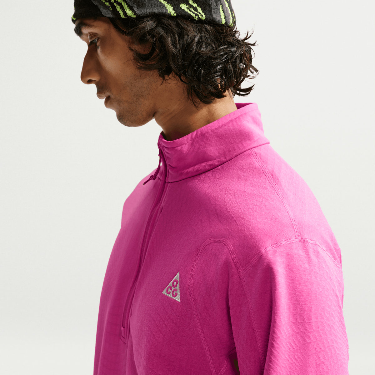 Men's Nike ACG Wolf Grid Therma-FIT 1/2 Zip Top Desert Pink Light Crimson Summit White side view on male trail runner showing lightweight packable grid fleece with flat seam construction for unrestricted mountain movement