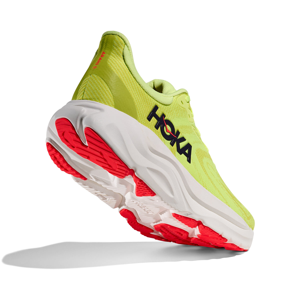 A yellow and white athletic running shoe with red accents, viewed from the back and slightly beneath, showing the shoes sole and the brand name HOKA on the side.