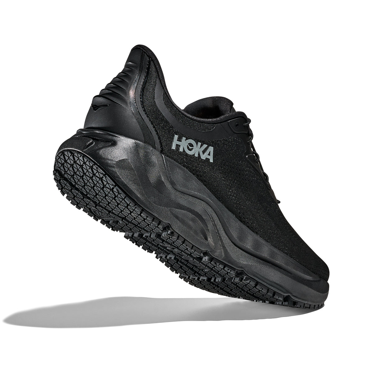 A black HOKA athletic shoe is shown from a side angle, with the sole facing forward and slightly upward. The shoe appears lightweight with a textured sole and visible HOKA logo on the side.