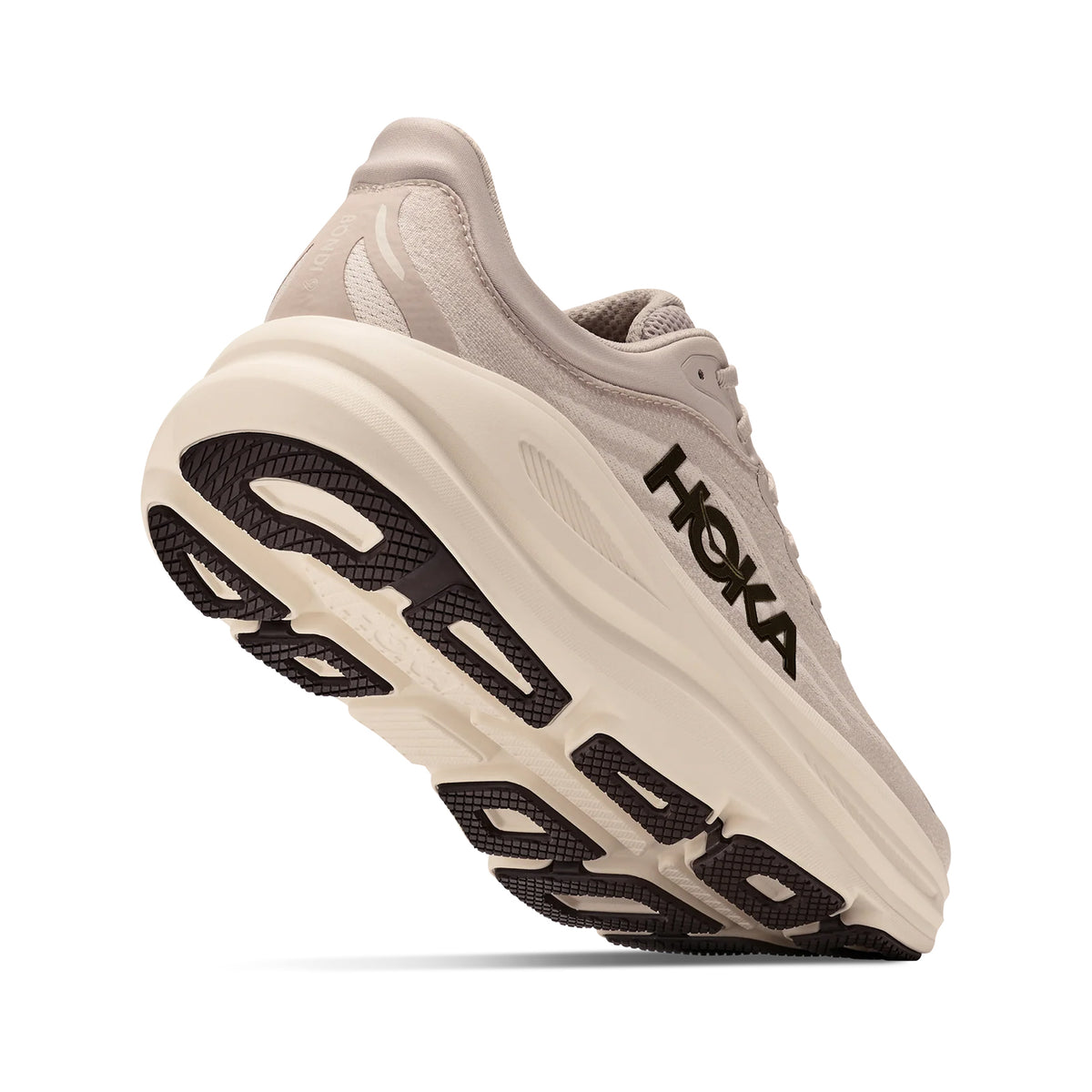 A beige HOKA running shoe is shown from a low angle, highlighting its thick, cushioned sole and black tread. The HOKA logo appears in black on the side of the shoe.