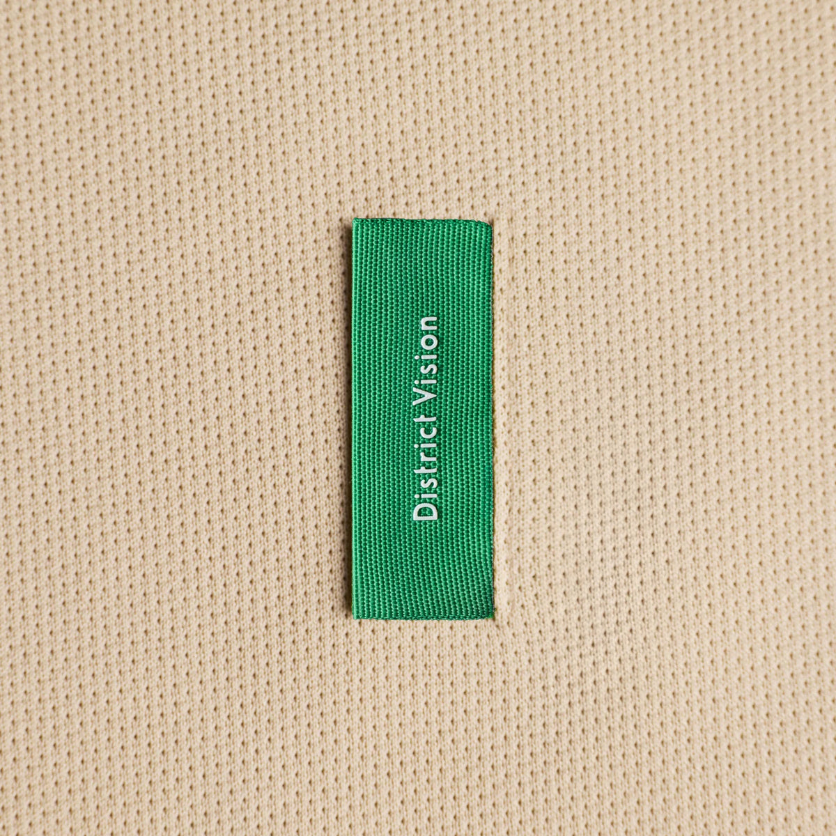 District Vision Short Sleeve Boxy Training Tee Beige close-up of custom woven label at lower right rib with barely-there feel construction