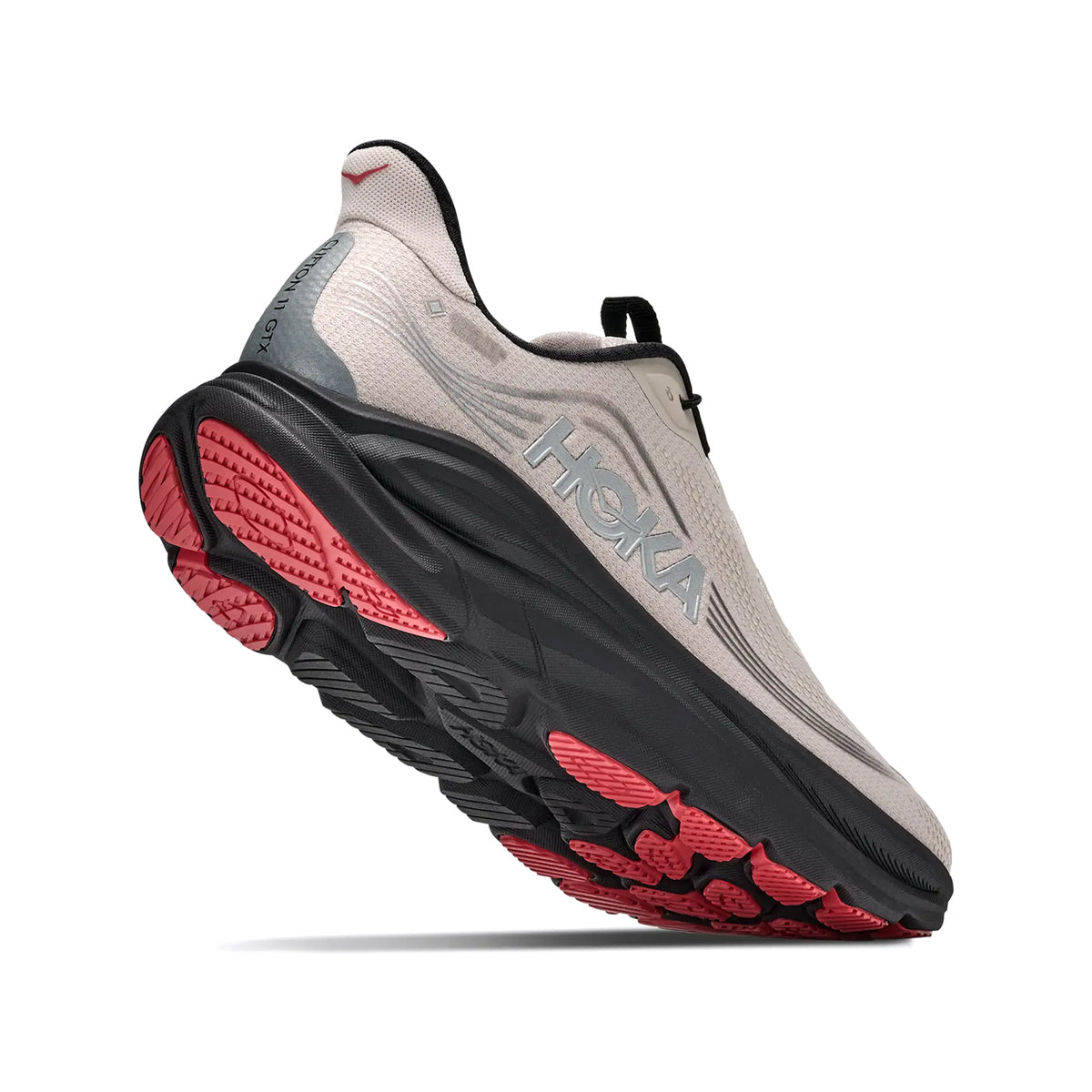 A beige HOKA running shoe with a thick black sole and red tread, viewed from a low angle highlighting the bottom and side design.