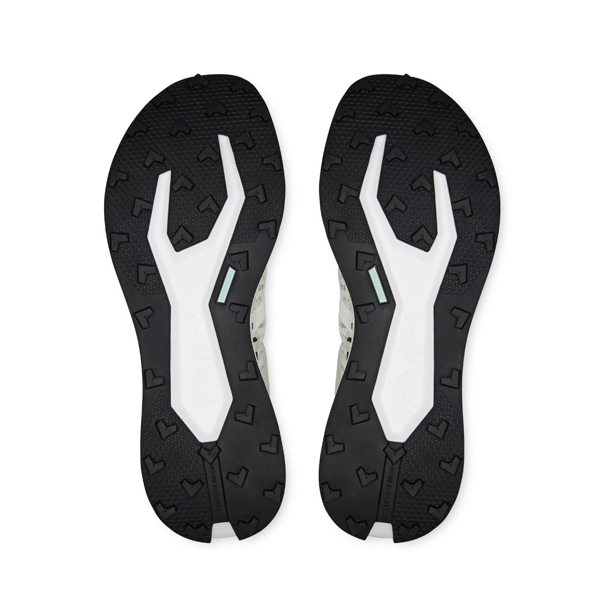 The image displays the black and white outsoles of the On Men’s Cloudultra Pro Trail Running Shoes in Ivory / Iceberg, featuring heart-shaped treads and geometric patterns designed to provide grip and traction on mountain terrain, as seen from the bottom.