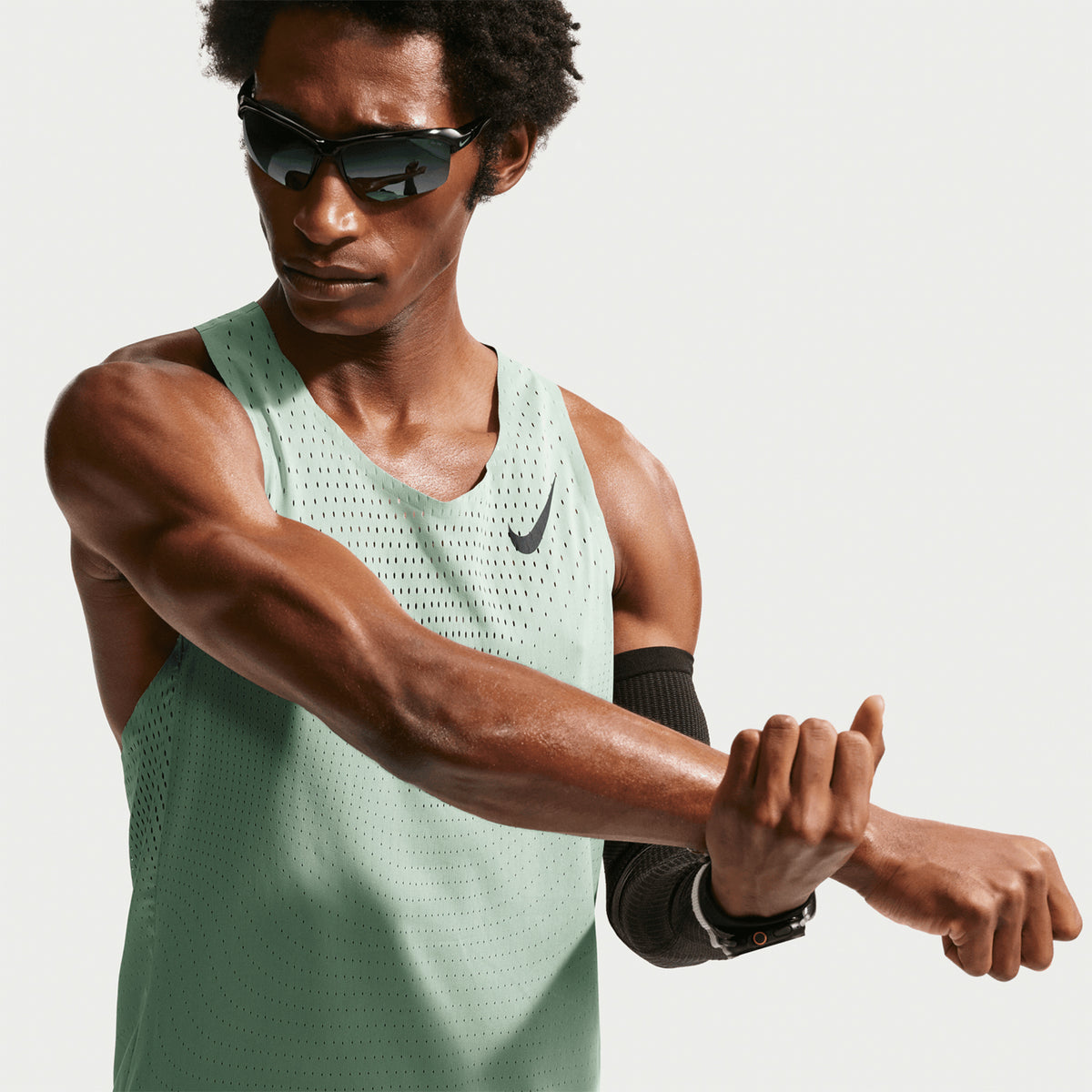Men's Nike Dri-FIT AeroSwift ADV Running Vest Green worn by male runner stretching showing smooth lightweight fabric, streamlined fit and freedom of movement for racing