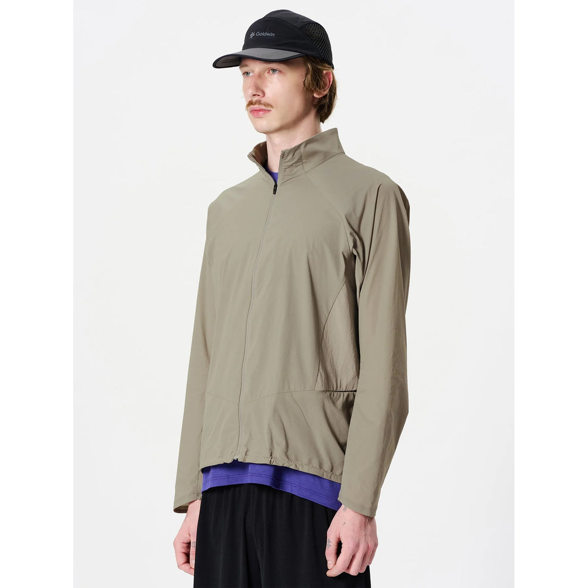 Goldwin Men's Eris Hybrid Jacket Arid Beige side view on male runner showing mesh panels from sides to armpits with stretch construction for natural movement