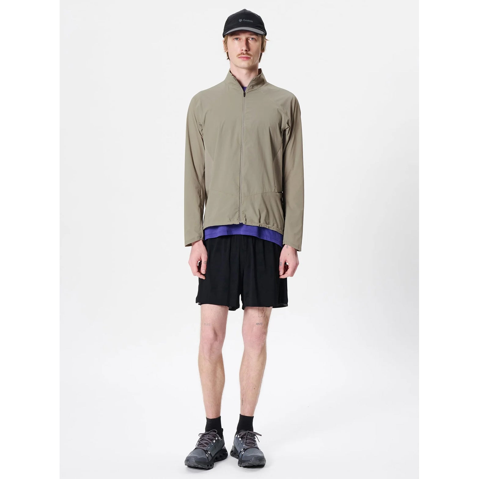 Goldwin Men's Eris Hybrid Jacket Arid Beige full body view on male runner showing strategic fabric placement with raglan sleeves for arm mobility