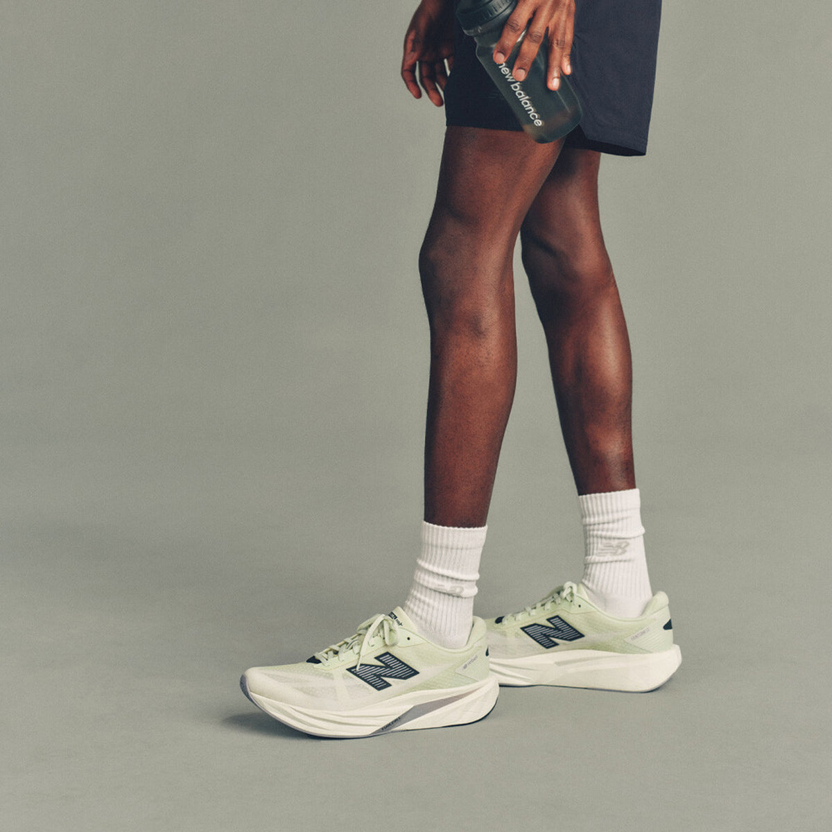 Men's New Balance FuelCell Rebel v5 Running Shoes Pistachio Butter Digital Mist side view on male runner showing FuelCell foam blend with bold geometric midsole for propulsive energetic feel across easy runs and tempo efforts