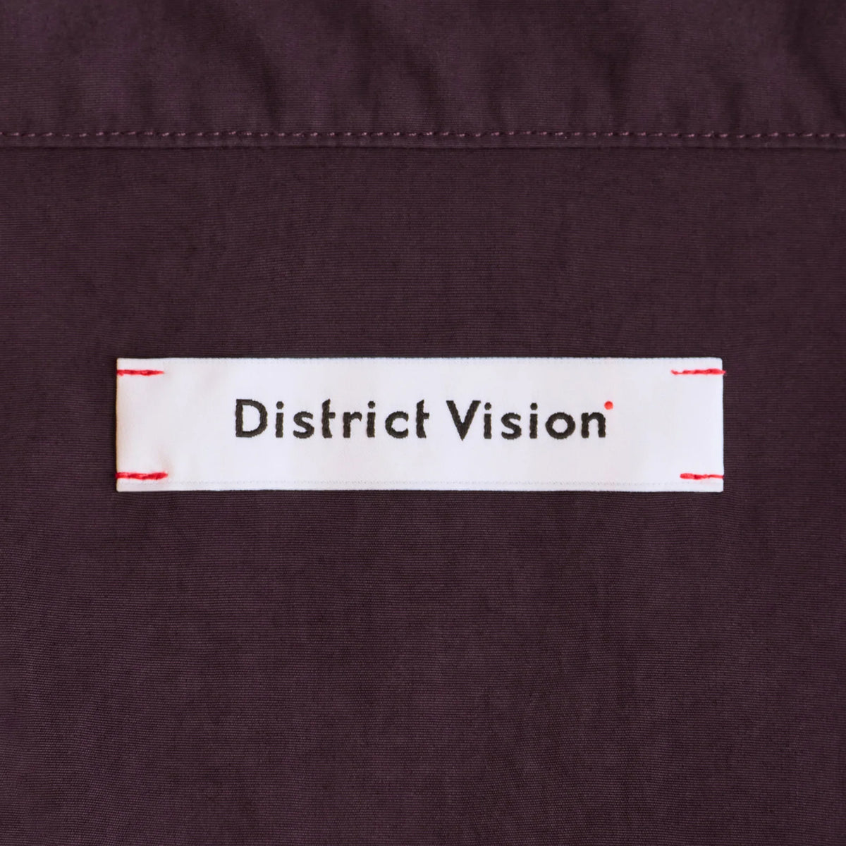 District Vision Men's Half Zip Nylon Windbreaker Blackberry close-up of custom woven label at shoulder functioning as integrated eyewear storage for securing sunglasses