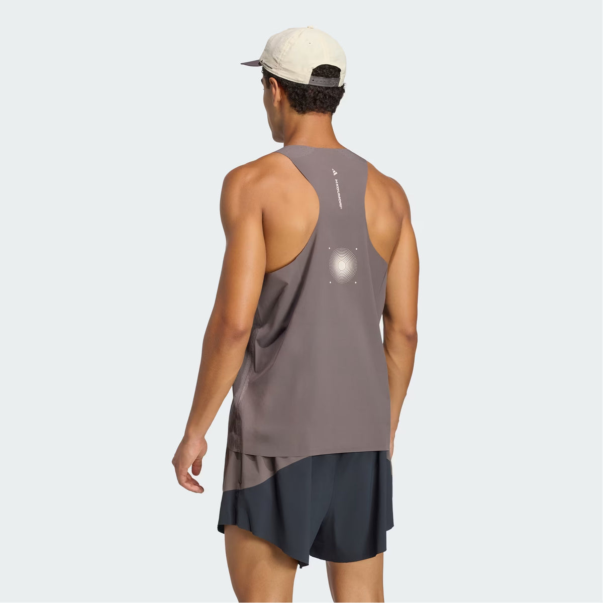 A man stands facing away, displaying the back of his performance running outfit and wearing the Adidas Men’s Hermanos Koumori Running Tank in Charcoal.