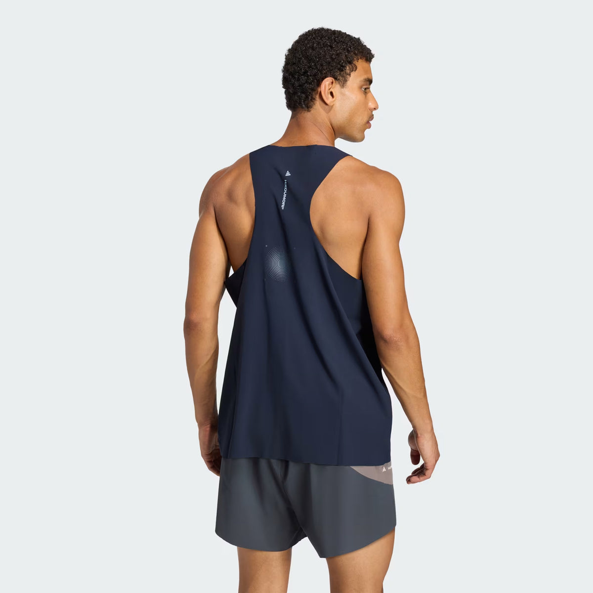 A man seen from behind wearing a navy blue Men’s Hermanos Koumori Running Tank and grey athletic shorts.