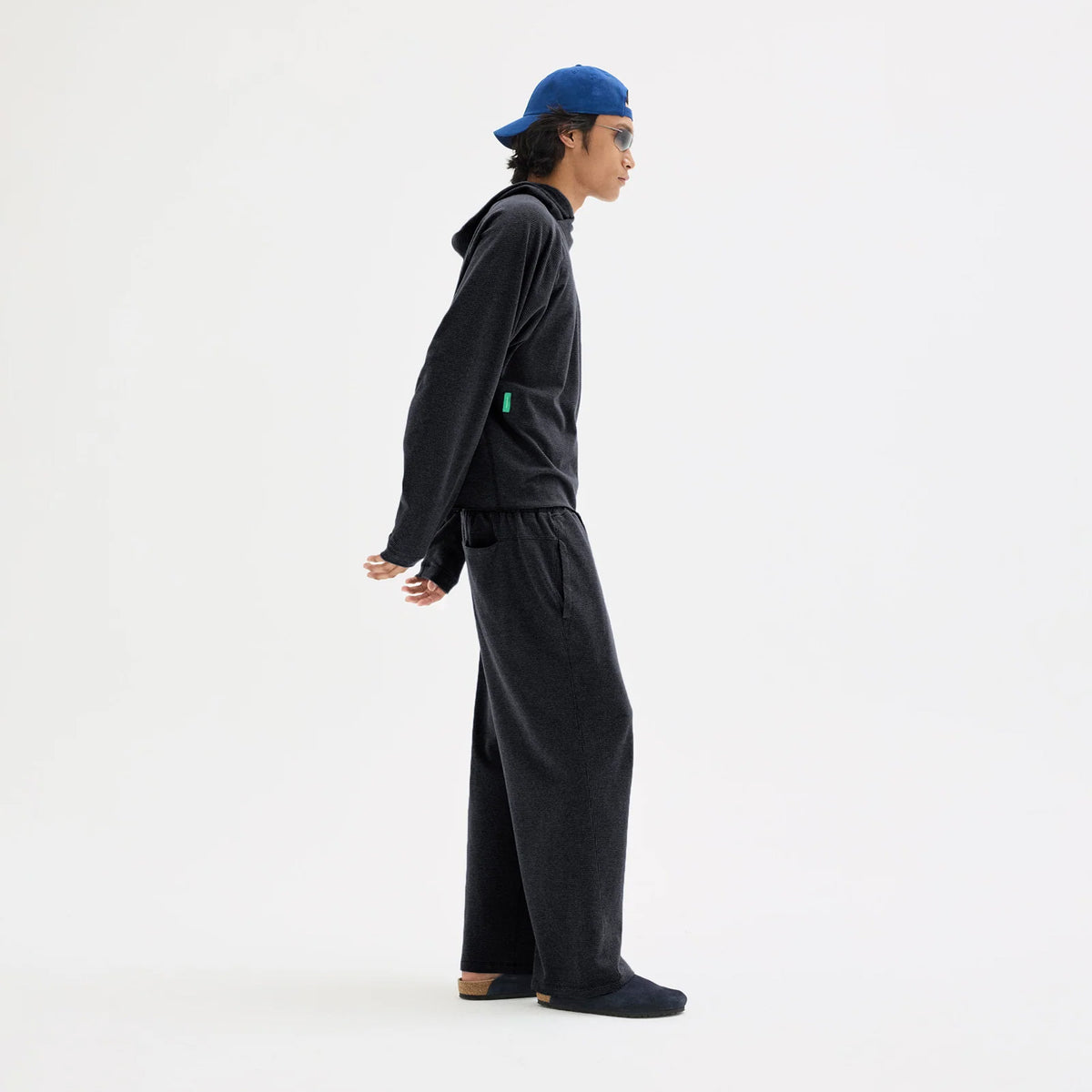 Person in profile wearing a Men’s Hooded Waffle Top Black, matching wide-leg trousers, a blue baseball cap, and sunglasses.
