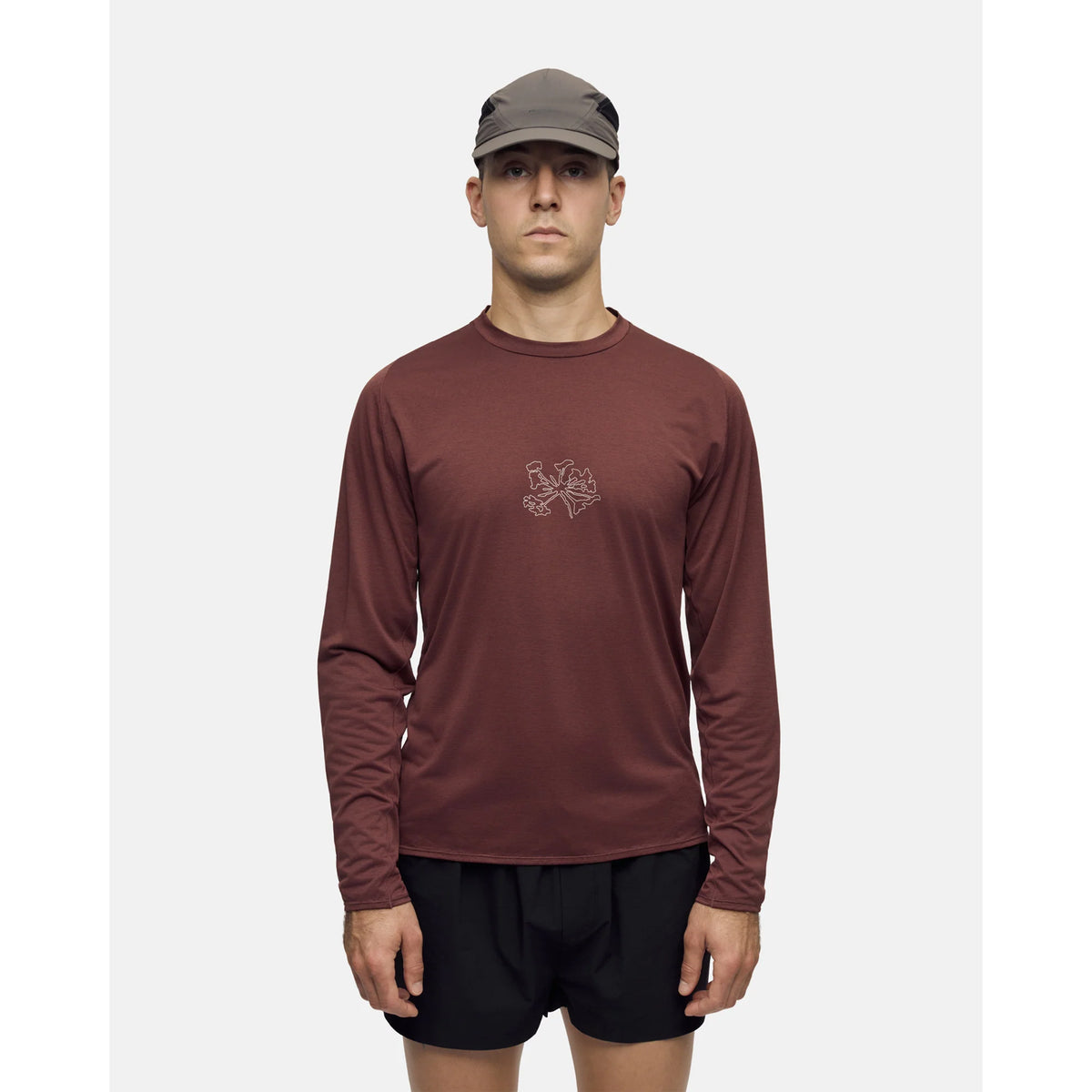 A man wearing a Portal Men’s Lateral Peak Long Sleeve Top Bitter Chocolate, black athletic shorts, and a grey cap.