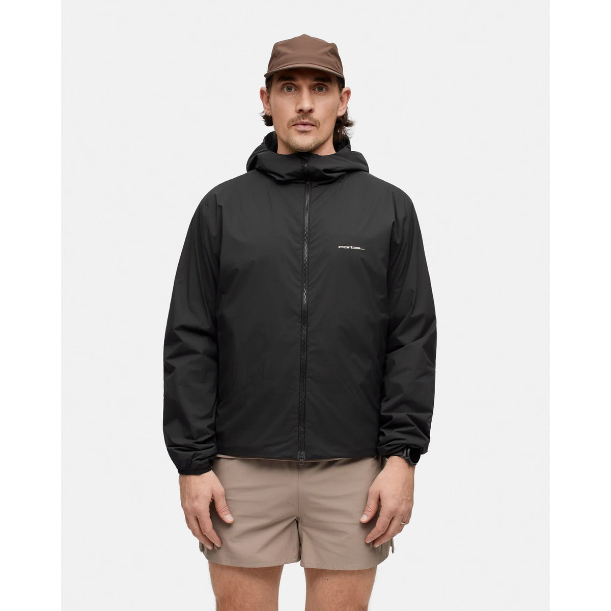 A man wearing a black Portal Men’s Level Alpha Jacket Black Beauty hooded zip-up jacket and khaki shorts.