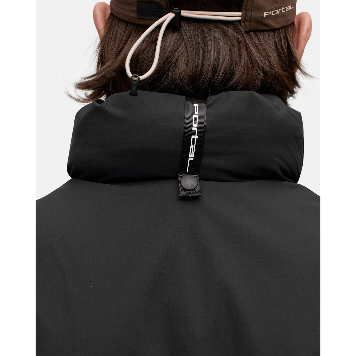 Back view of a person wearing a black Men’s Level Alpha Jacket Black Beauty by Portal, featuring a tall collar with a vertical branded pull tab.