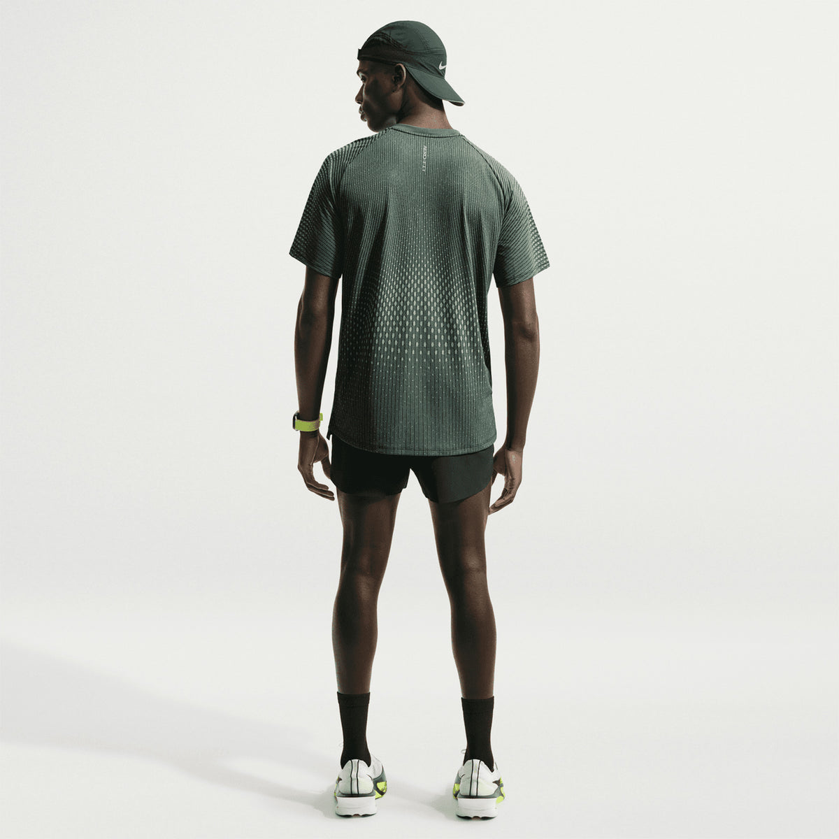 Men's Nike Stride Aero-FIT Running Tee Black Light Green Spark full body back view on male runner showing strategic back mesh zones with Aero-FIT technology for maximum breathability and active cooling during warm weather training