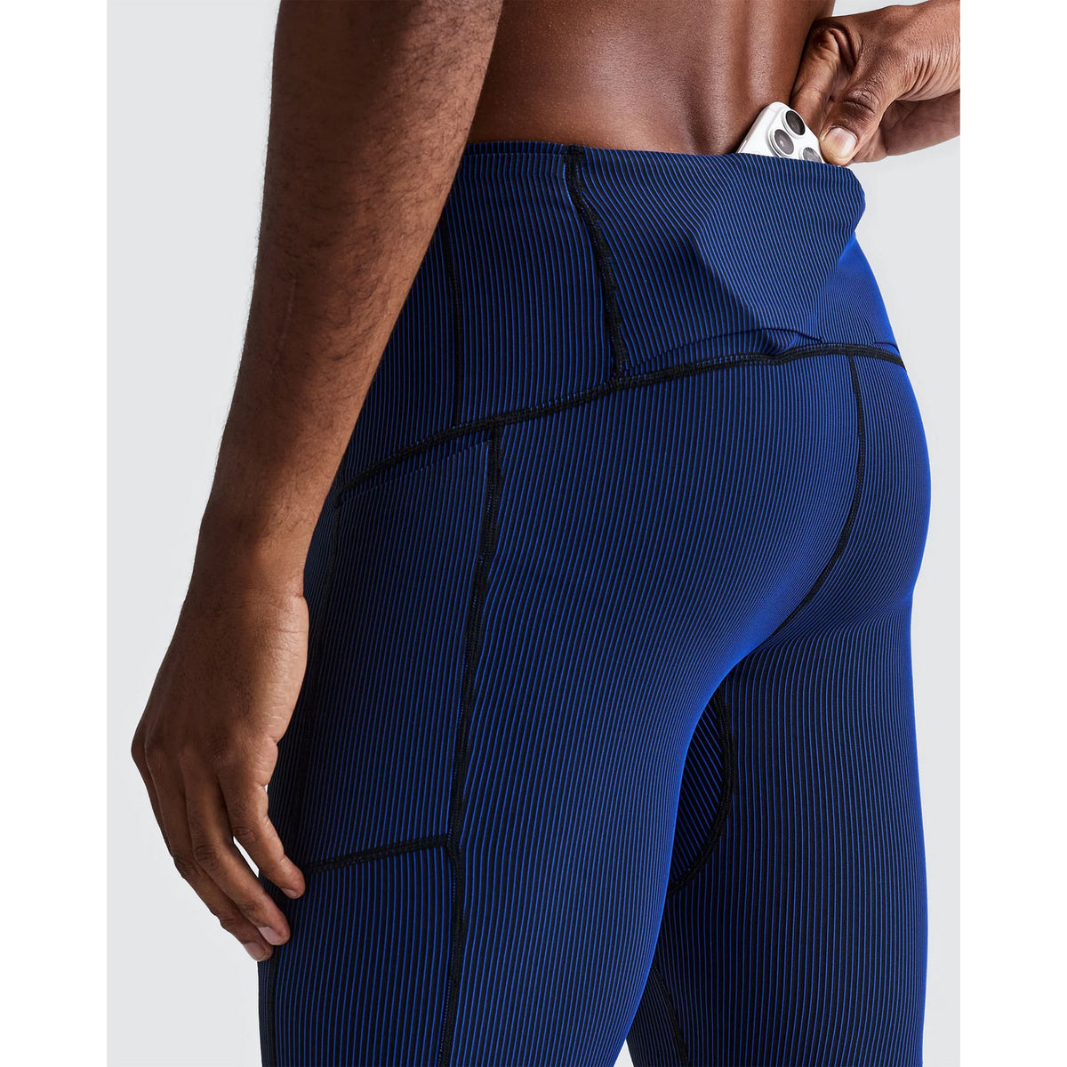 A person sliding a smartphone into a rear waistband pocket of Bandit Men’s Striped Cadence Half Tights Black / Bauhaus Blue.