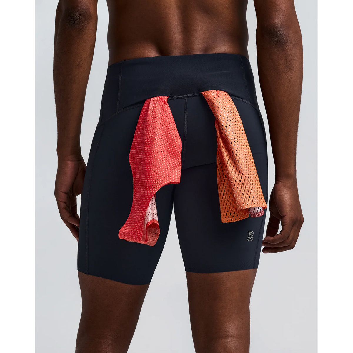 A person wearing Bandit’s Men’s Vanisher Half Tights Anthracite, which feature a seven-pocket system, stands facing away with two mesh towels—one red and one orange—tucked into the waistband at the back.