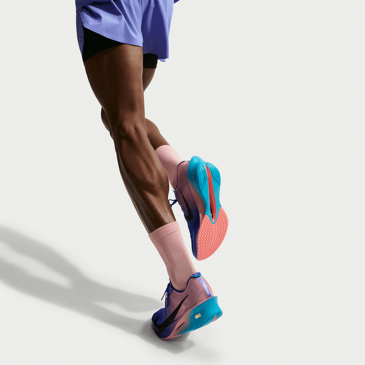 Men's Nike Vaporfly 4 Running Shoes Racer Blue Blue Lightning Atomic Pink White sole view on male runner showing thinner rubber outsole with full-length carbon Flyplate for lightweight propulsive race day traction