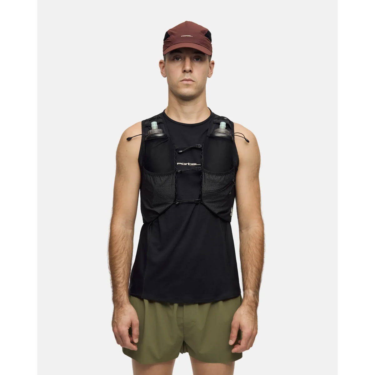 A person wearing a maroon cap, black sleeveless shirt, olive green shorts, and the Portal Passage Cargo Vest in Black Beauty with two water bottles, standing against a plain light background.