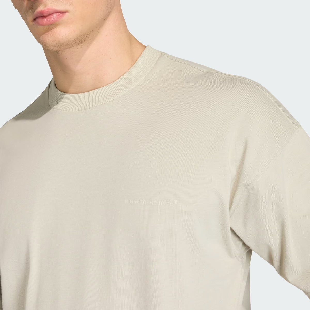A person wearing the Adidas Unisex Adi365 H.Koumori Running Tee in Putty Grey is shown from the shoulders to mid-chest against a neutral background. Their face is partially visible, and the cotton running shirt features no prominent logos or graphics.