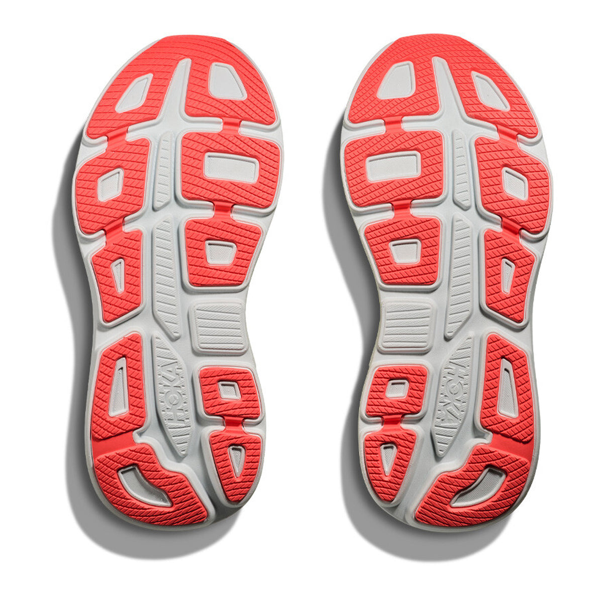 Two athletic shoe soles are shown from the bottom, featuring a white base with bright red, textured rubber sections and geometric tread patterns for enhanced traction. The word “HOKA” is visible on each sole, highlighting the signature design of the Hoka Women’s Bondi 9 Running Shoes in Neon Yuzu / Sunlight—ultra-cushioned and built for all-day comfort. Shadows appear on the left.