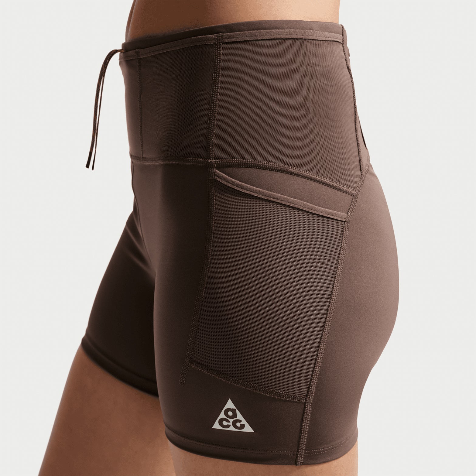Women's Nike ACG High-Waisted 4 Inch Short Tights Ironstone Cave Stone Summit White side view on female runner showing 4-inch inseam with mesh drop-in side pockets, waistband gel storage and Dri-FIT sweat-wicking fabric for trail running
