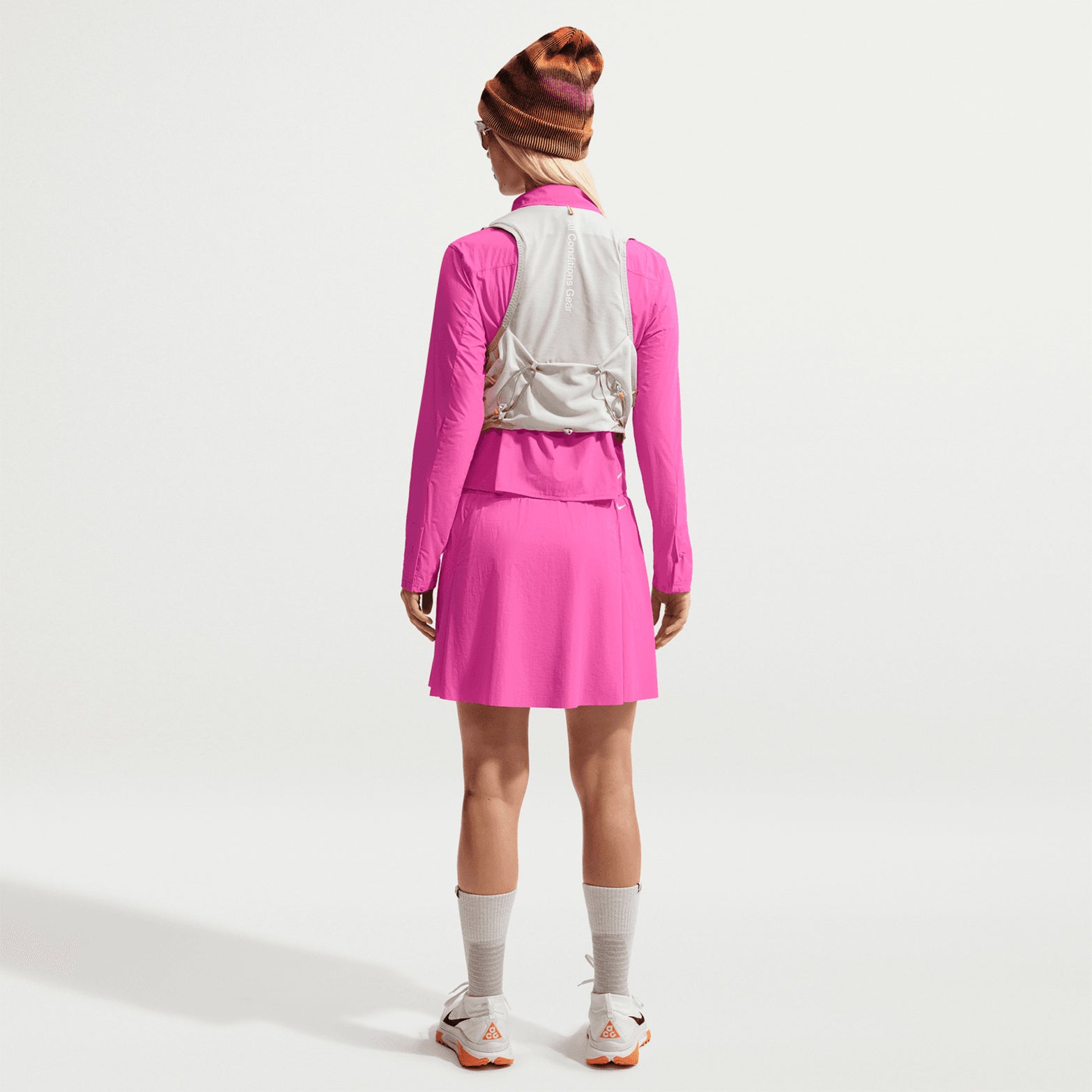 Women's Nike ACG High Stakes Skort Desert Pink Light Crimson Summit White back full body view on female trail runner showing zippered back pocket with lightweight stretch-woven construction and wide stretchy waistband for comfortable mountain hiking