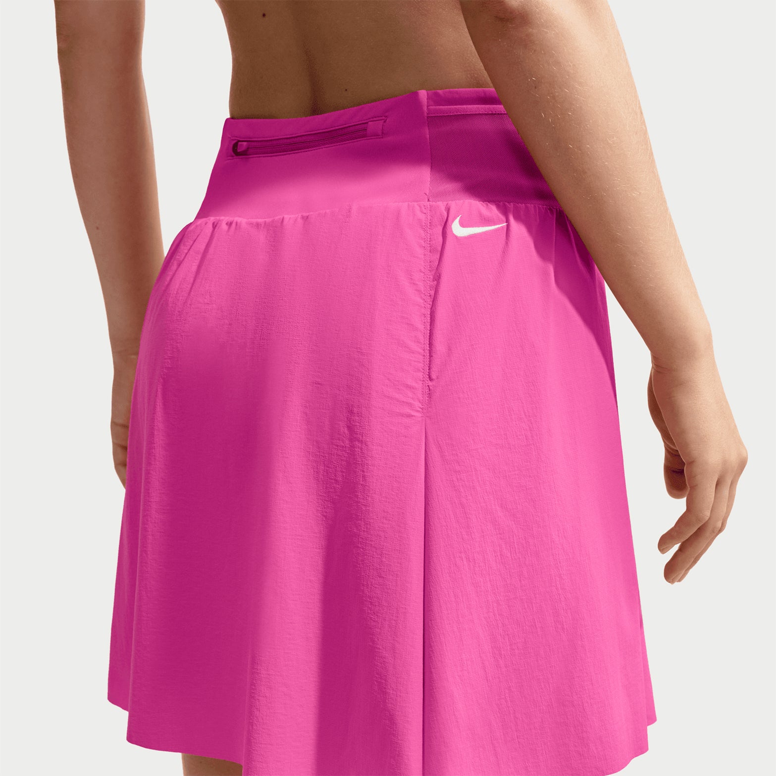 Women's Nike ACG High Stakes Skort Desert Pink Light Crimson Summit White back view on female trail runner showing zippered back pocket with stretch-woven construction and UV protection for mountain activities