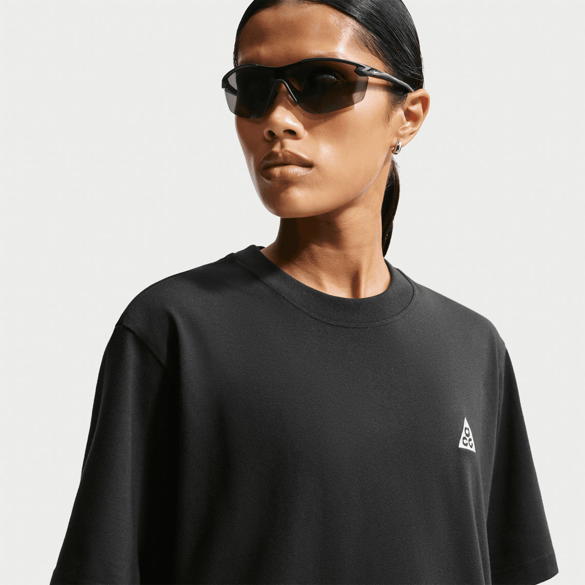 Nike ACG Tee women's in Black / Summit White — front closeup worn on model with sunglasses showing black knit fabric detail, summit white accent detailing and sustainable recycled polyester and organic cotton construction