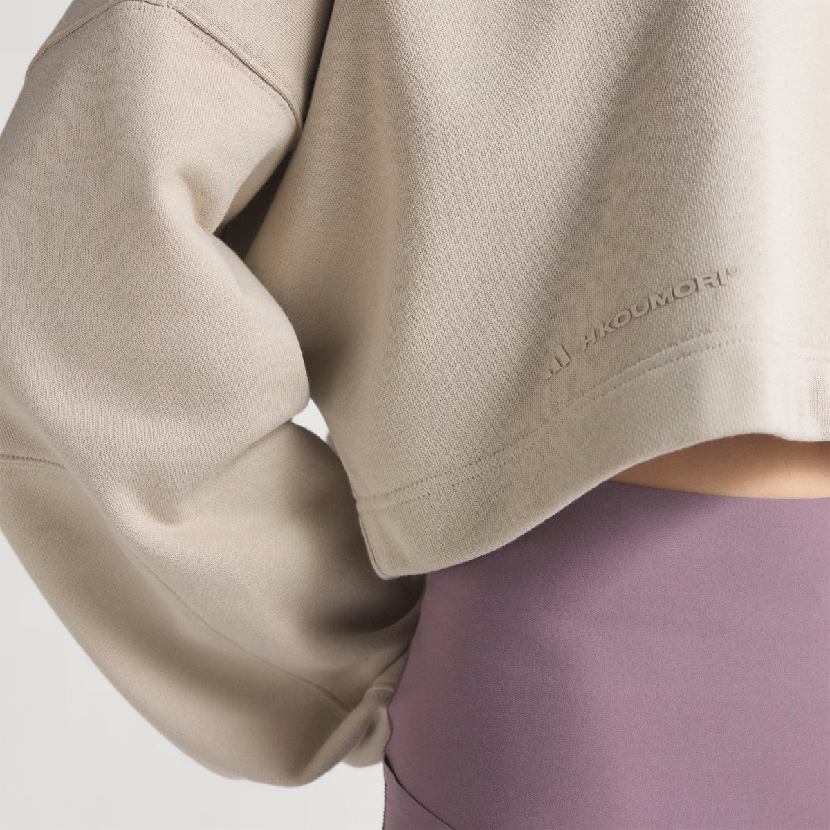 A person wearing the Adidas Women’s Adi365 H.Koumori Running Crew Top in Putty Grey, styled with high-waisted lavender leggings; only the torso and part of one arm are visible.