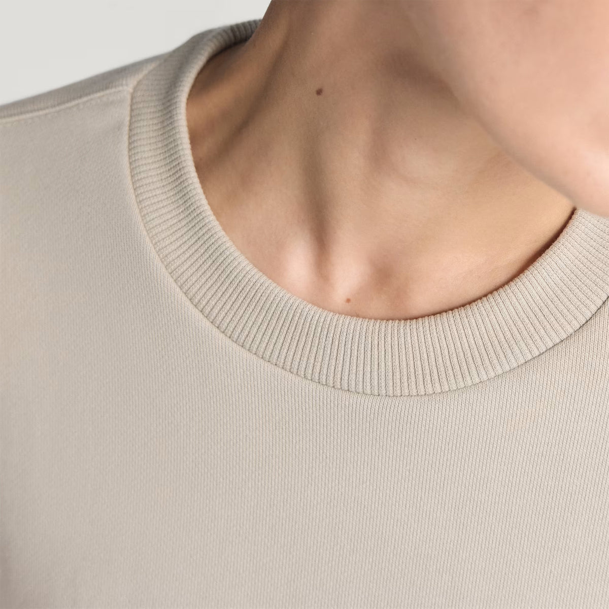 Close-up of a person’s neck and shoulder wearing the Adidas Women’s Adi365 H.Koumori Running Crew Top in Putty Grey. The image highlights the streetwear-inspired ribbed texture and fabric detail, with most of the person’s face out of frame.