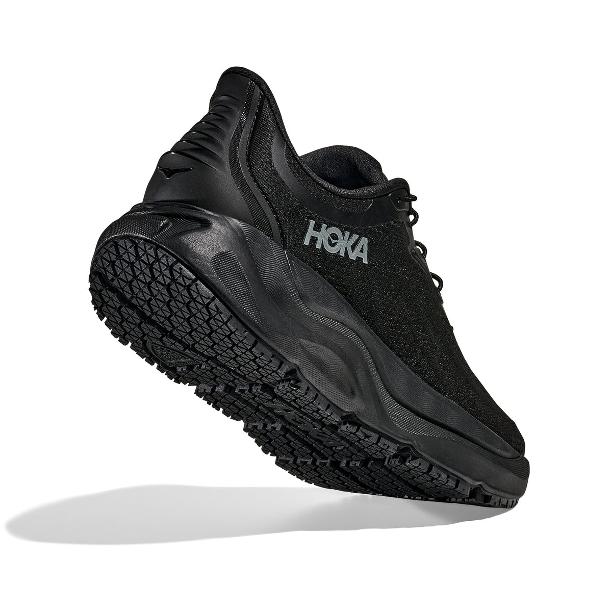 A black HOKA running shoe is shown from a rear side angle, highlighting its textured sole and cushioned heel. The shoe is photographed on a white background with a faint shadow underneath.