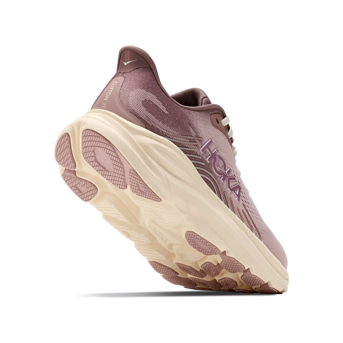 A mauve and cream running shoe is shown from a low rear angle, highlighting its thick cushioned sole, textured outsole, and the brand logo on the side.