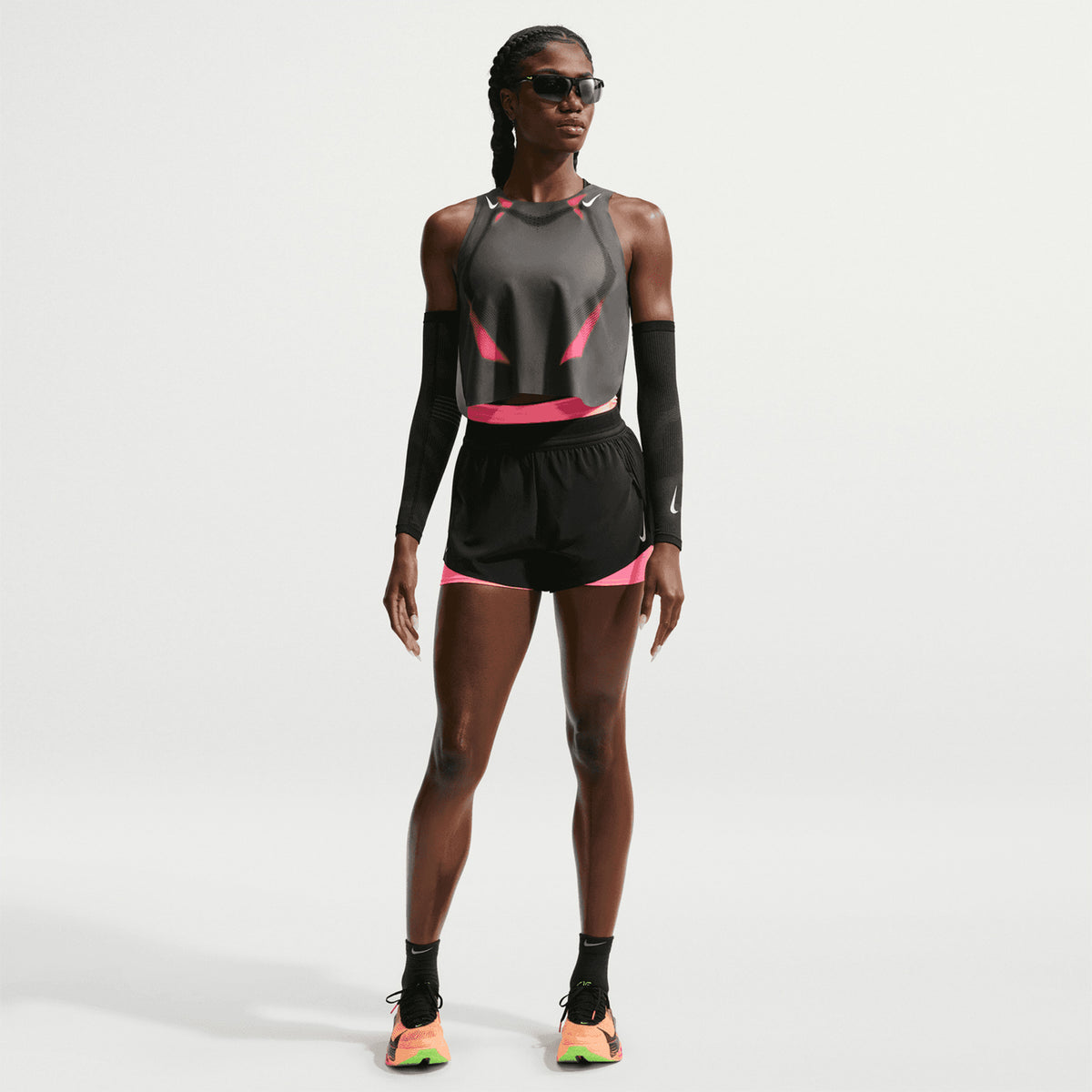A woman stands confidently against a plain white background wearing a Nike Women’s Dri-FIT ADV Cropped Vest in Iron Grey, Volt, and White.