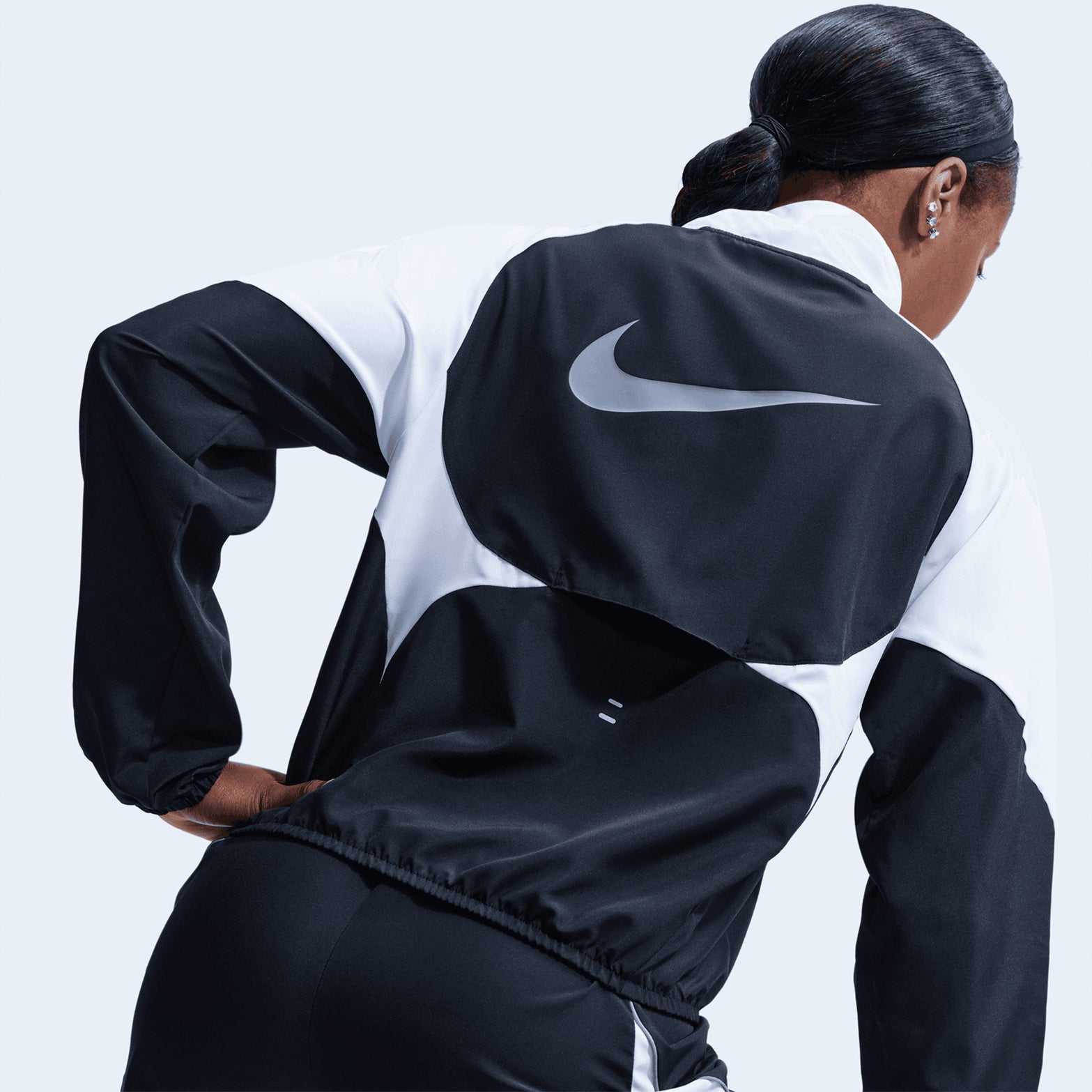 A person is seen from behind wearing the Nike Women’s Dri-FIT Tempo Swoosh 1/2 Zip Running Jacket in Black, White, and Cool Grey, with the prominent Nike logo displayed on the back of this ultralight running jacket.