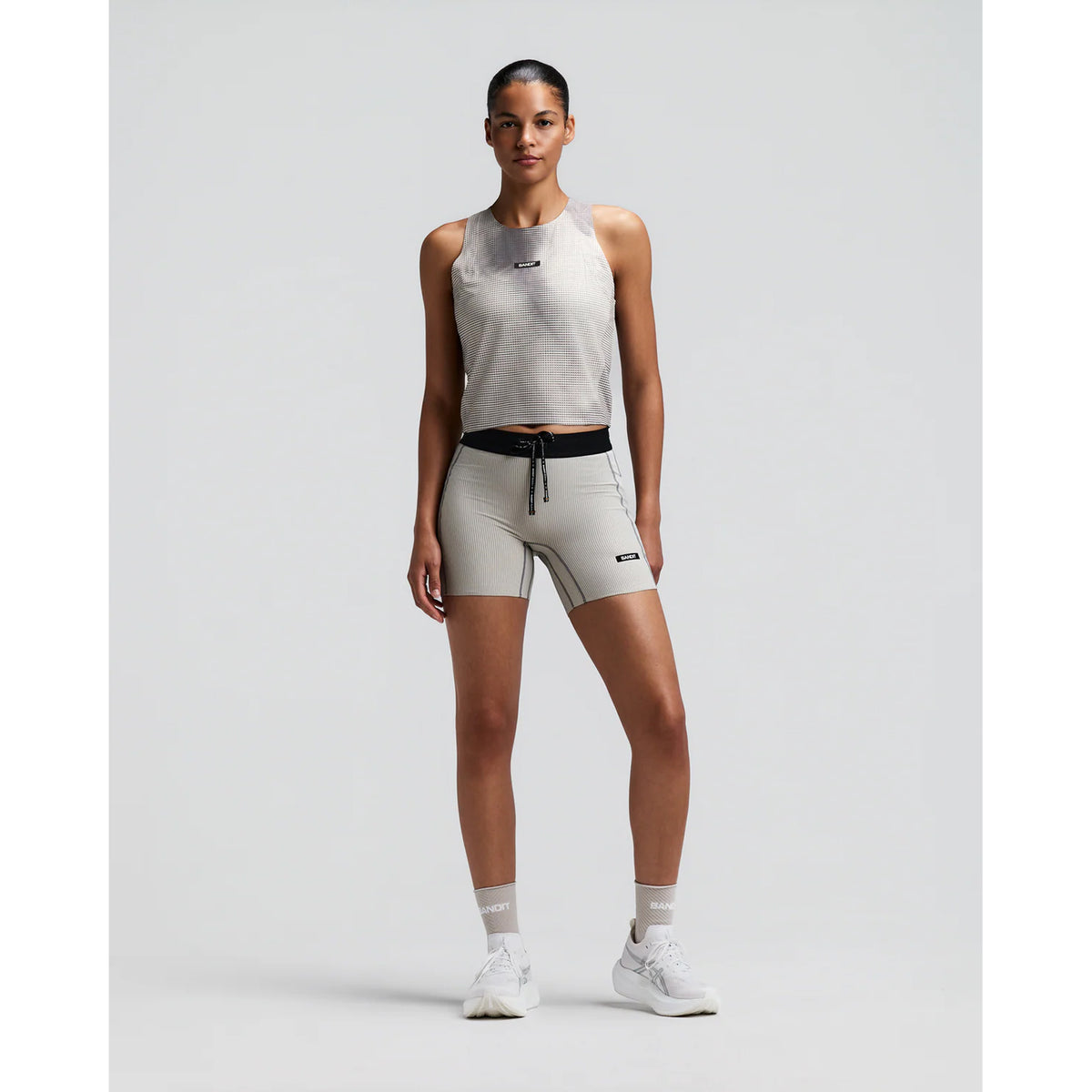 Women's Bandit GeoMesh Race Singlet Slate Plaster front full body view on female runner showing cropped hip-length design with GeoMesh breathable performance knit and bonded seam finishing for racing and fast training