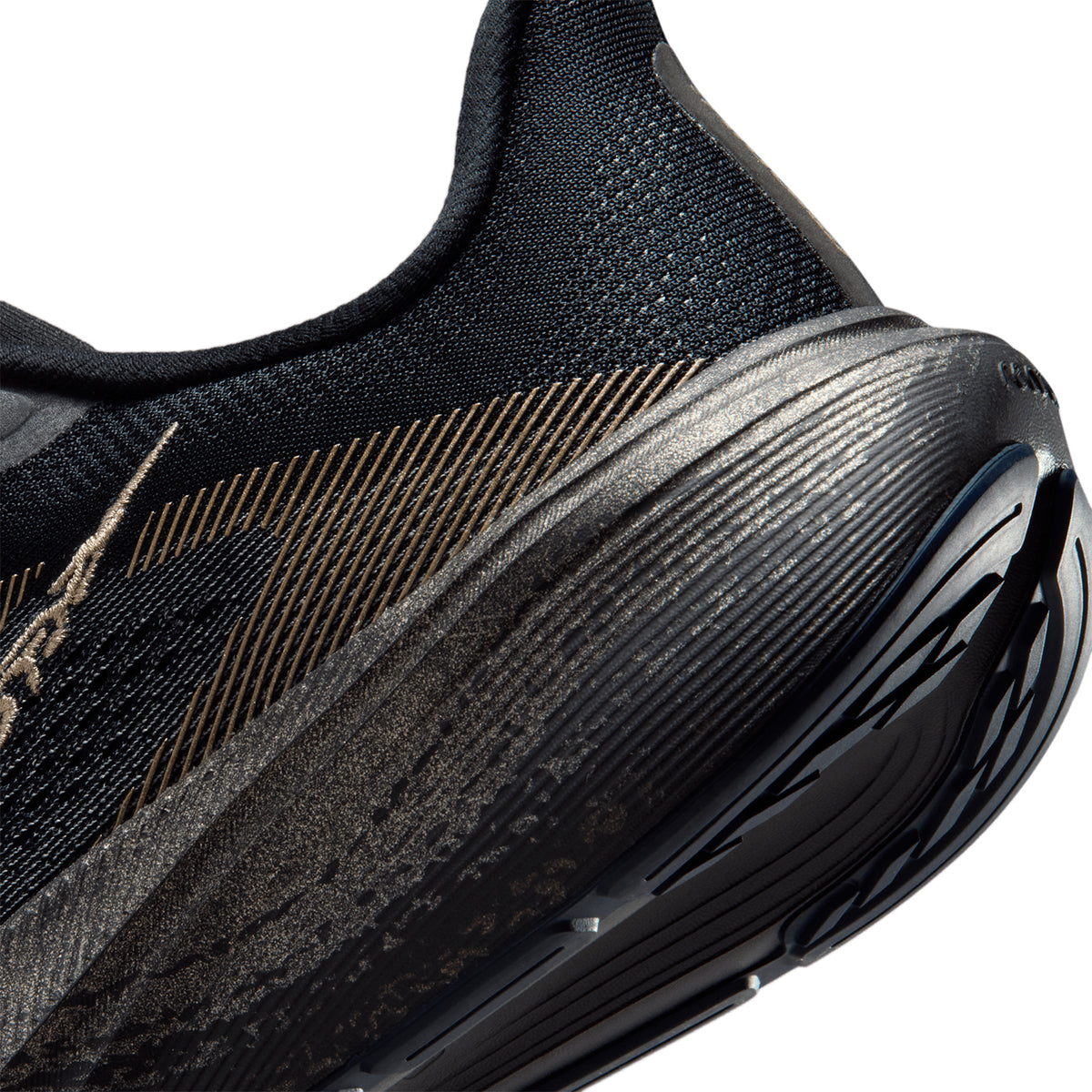 Close-up of a black athletic shoe with gold accents, showing the heel, textured mesh upper, and detailed sole pattern.